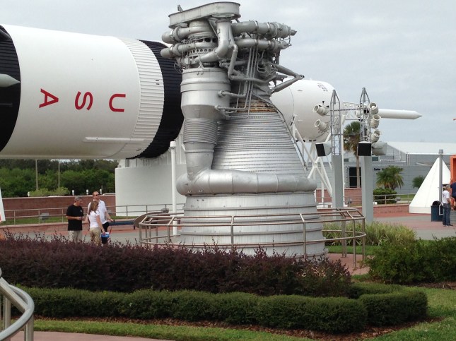 One Saturn V engine beside a six foot tall man. The smaller Saturn 1B is in the background